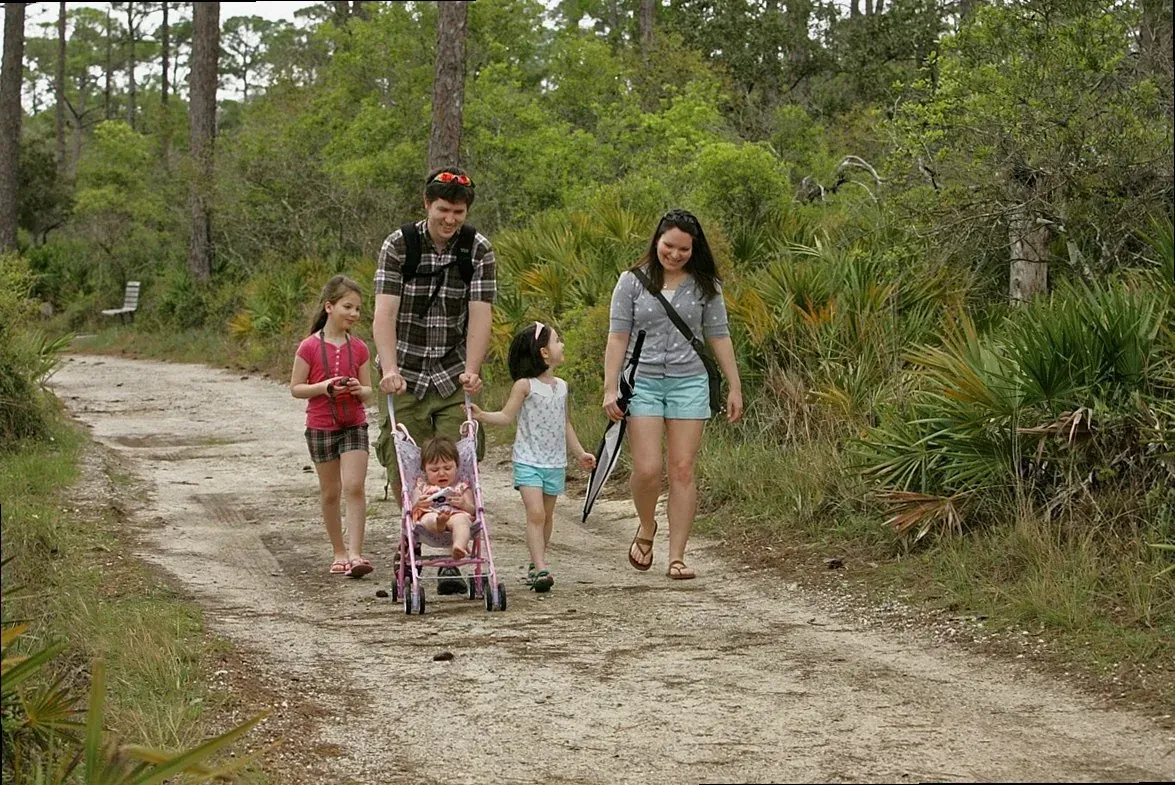 A family walking together along a sandy woodland trail during a portrait session