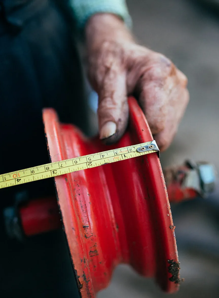 A maker measuring a wheel rim by hand with a tape measure