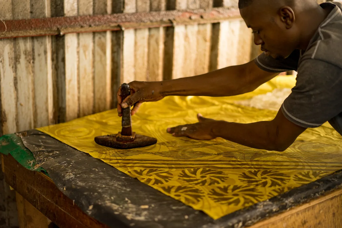 A craftsman hand-stamping a repeating pattern onto yellow cloth at the workbench